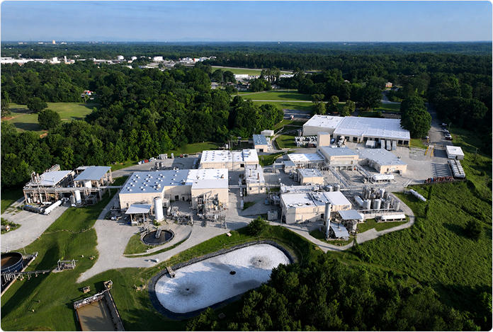 Aerial view of a large chemical manufacturing campus with multiple buildings and a treatment pond.